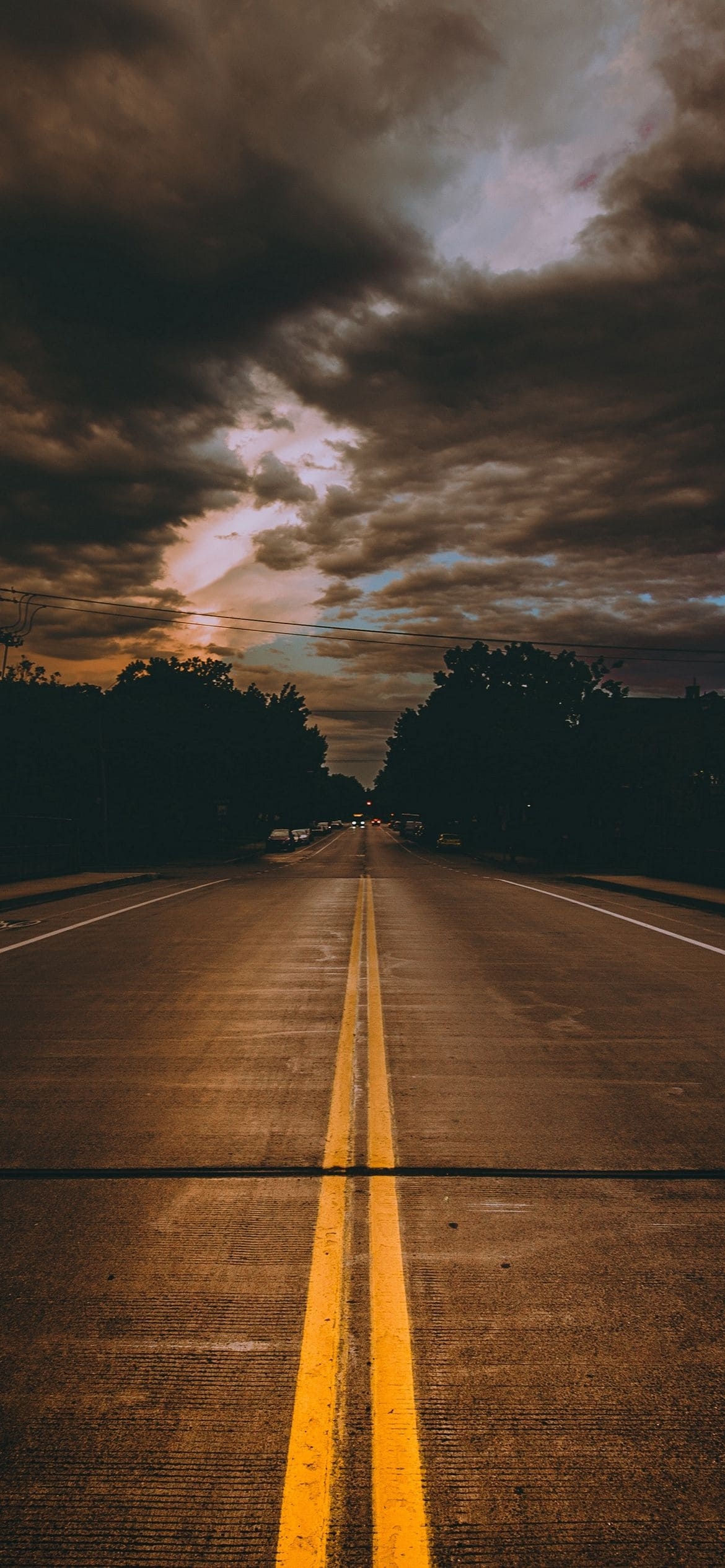 両脇が緑の林に囲まれた道路と曇り空の1170 x 2532 / スマホ壁紙