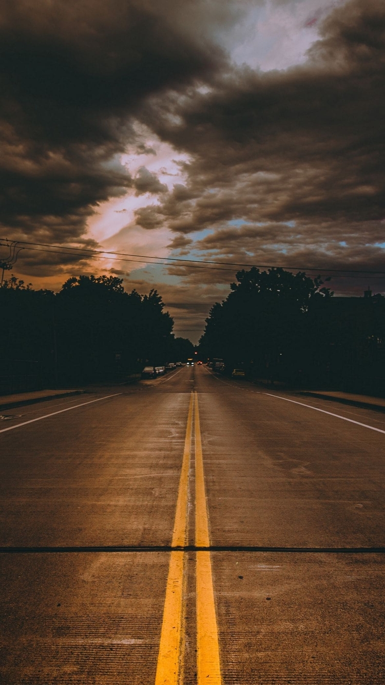 両脇が緑の林に囲まれた道路と曇り空の750 x 1334 / スマホ壁紙