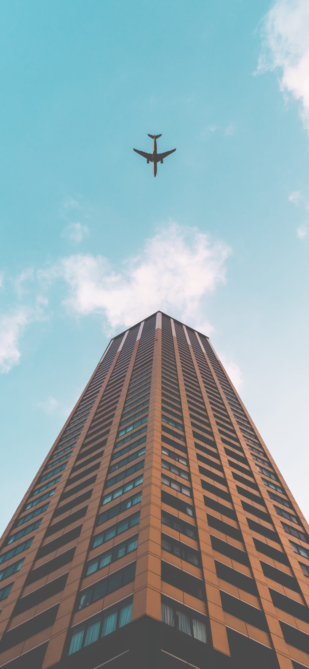 下から見上げる茶色い高層ビルと飛行機の1170 x 2532 / スマホ壁紙